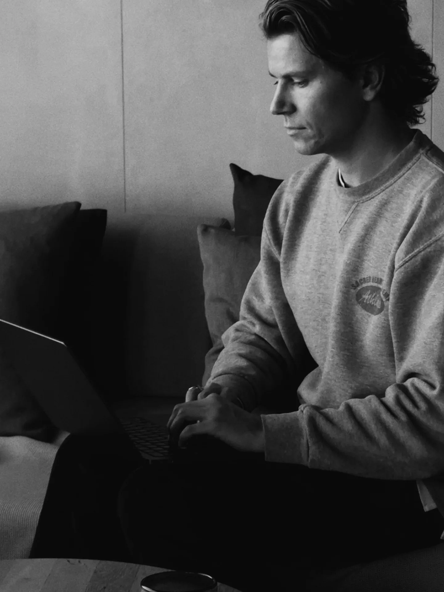 Julius at work on a laptop on a sofa in the studio. Black and white.