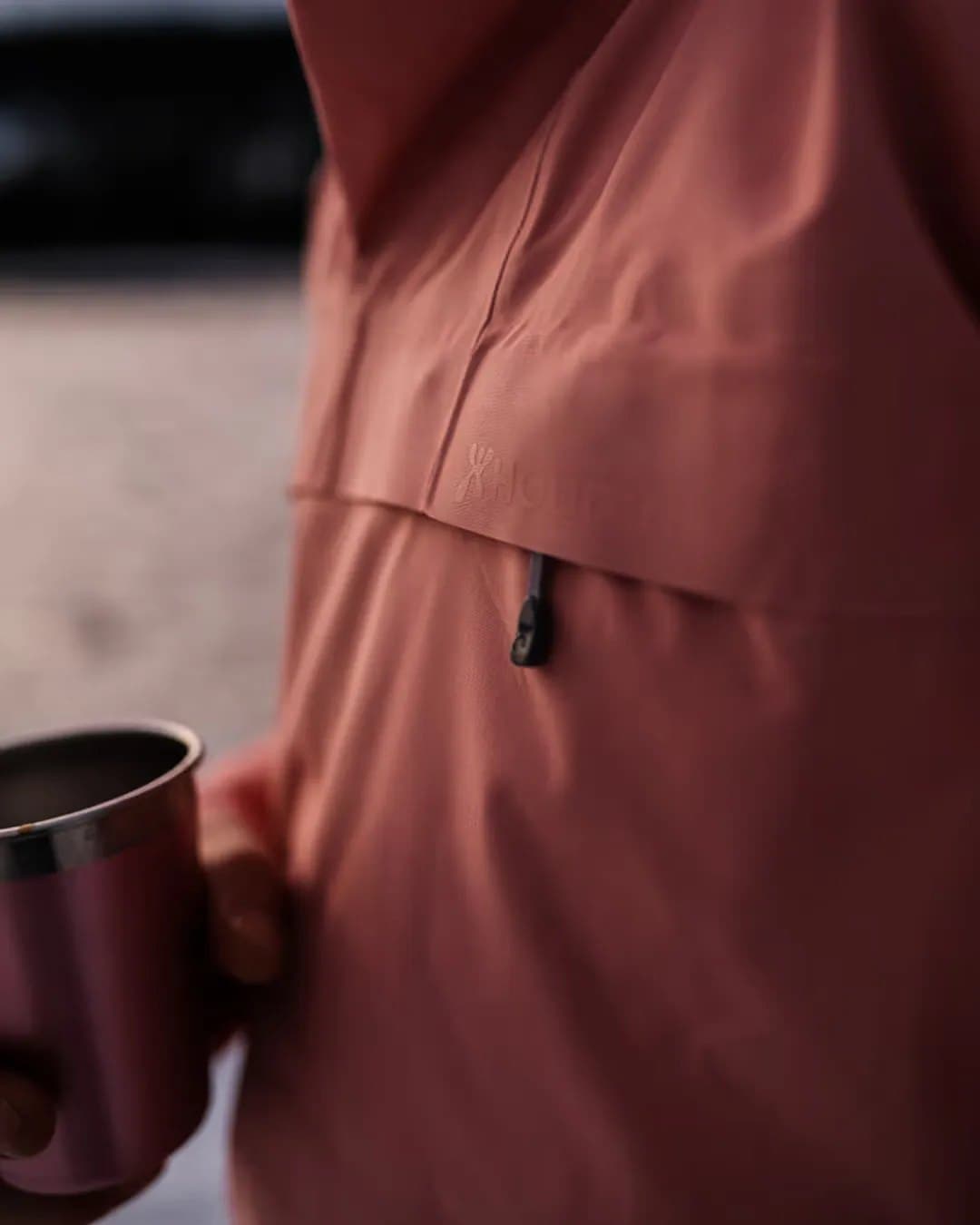 A hand holding a cup against a coral jacket. Photo: Petter Bülling.